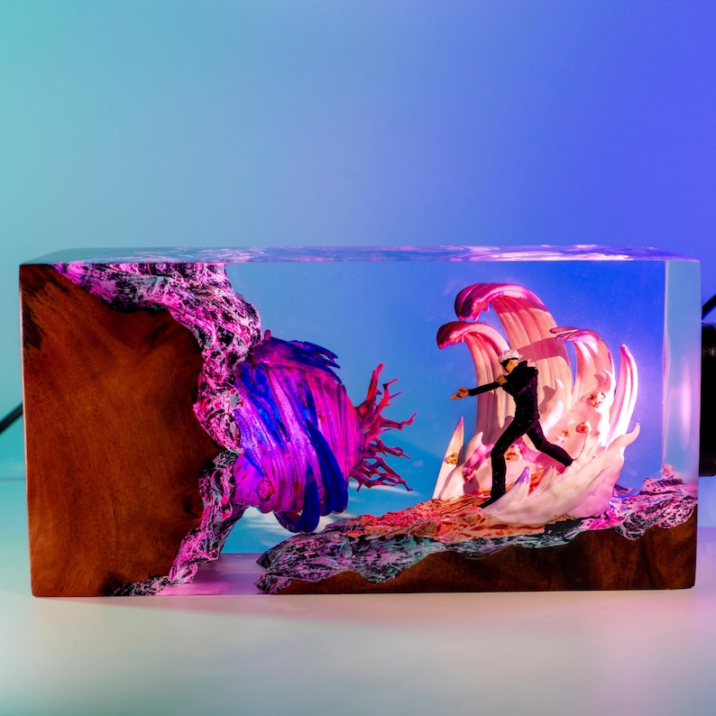 May include: A decorative resin block featuring a miniature scene of a figure in a sailor's uniform facing a large wave. The scene is set against a blue sky backdrop, with wood and coral accents. The block measures approximately 6 inches long.