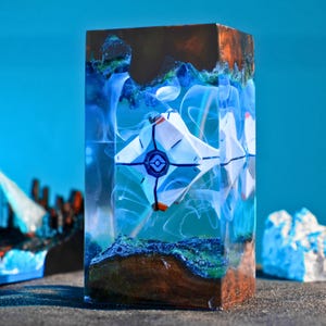 Può includere: Un'opera d'arte rettangolare in resina con un design geometrico bianco e blu racchiuso in resina trasparente. Il pezzo ha una base marrone scuro con accenti verdi e blu, su sfondo blu.