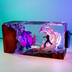 May include: A rectangular resin art piece featuring a miniature figure in a dynamic pose, set against a backdrop of stylized waves and abstract forms. The piece has a wooden base and a vibrant color palette of purple, blue, and white.