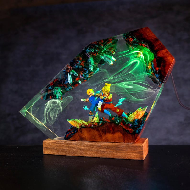 Pu&ograve; includere: Una lampada decorativa con due figure anime in posa dinamica, racchiuse in un blocco di resina trasparente con legno ed elementi cristallini. La resina emette una luce verde brillante, creando un effetto di fumo vorticoso attorno alle figure.
