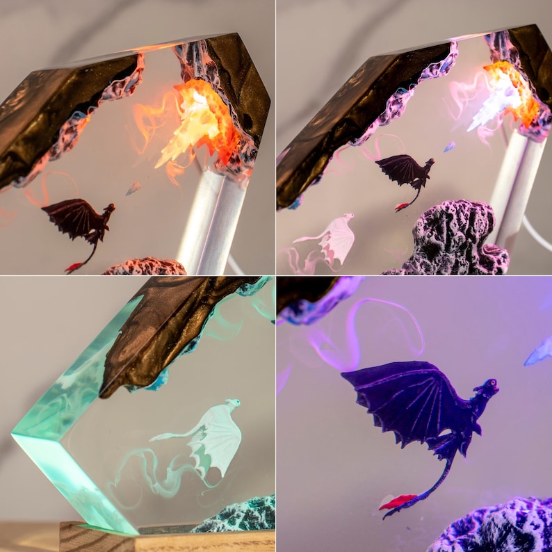 May include: A decorative resin lamp featuring a hexagonal frame with embedded dragon figures. The design includes a black dragon with red tail accents and a white dragon, set against a translucent background with internal lighting that shifts between orange, purple, and teal hues.