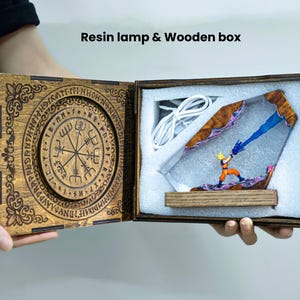 May include: A resin lamp and wooden box set featuring a miniature figure of a character with spiky yellow hair firing a blue energy beam. The wooden box lid is engraved with a circular runic design, and the interior contains white foam padding.