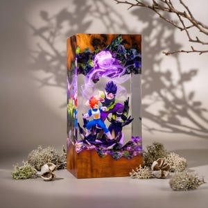 Op de afbeelding: Een rechthoekige hars- en houten lamp met twee anime-figuren in een dynamische gevechtshouding. Het heldere harsgedeelte bevat wervelende paarse lichteffecten en donkere getextureerde elementen, terwijl de basis en bovenkant van gepolijst bruin hout zijn.