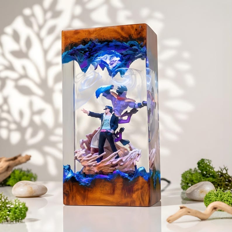 May include: A rectangular resin lamp featuring a detailed anime scene. The lamp has a wooden base and a clear resin body with blue and purple accents. The scene depicts two figures in action poses, with one figure in a black coat.