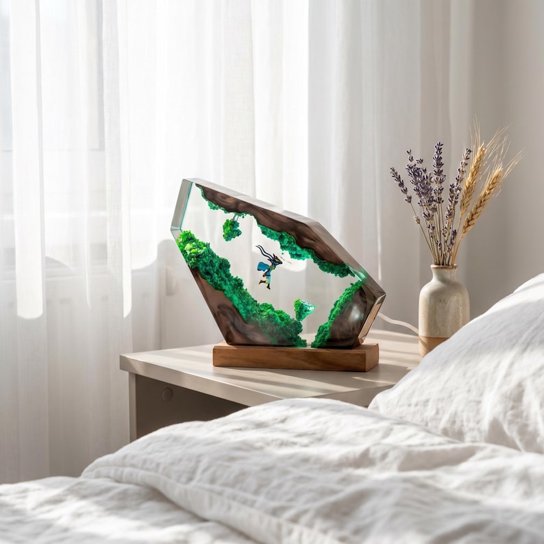 May include: A decorative lamp featuring a clear resin block with embedded dark wood, vibrant green moss, and a small figurine of a character in a blue outfit. The lamp is mounted on a rectangular wooden base and emits a soft internal light.