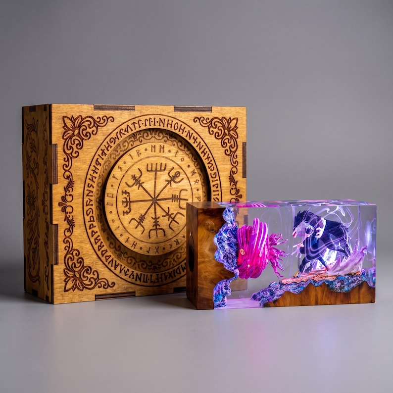 May include: A square wooden box featuring an engraved circular Viking compass design and a rectangular resin block containing a miniature scene with a glowing pink creature and a dark figure, illuminated by internal purple and blue light effects.