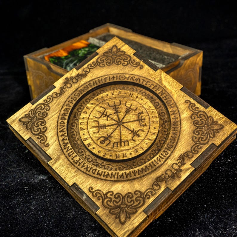 May include: A square wooden box with a removable lid featuring a laser-engraved Vegvisir symbol surrounded by a circular border of runic characters. The corners of the lid are decorated with intricate scrollwork patterns in a dark brown finish.