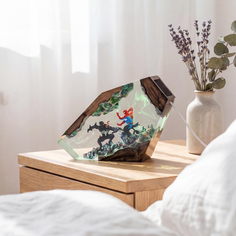 May include: A decorative lamp featuring a scene with superhero figures encased in a clear, geometric resin block. The lamp has a wooden frame and is illuminated with green and white light. It sits on a wooden nightstand.