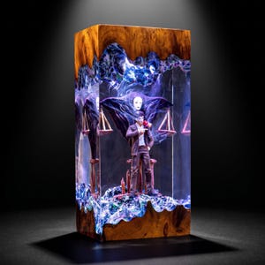 May include: A rectangular block made of natural wood and clear resin, featuring an internal diorama of a figure in a brown suit standing before a scale. The resin contains swirling blue and white patterns, illuminated from within by light.
