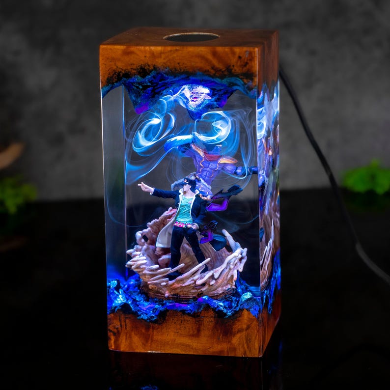 May include: A rectangular resin lamp with a wooden top and base. The lamp features a figurine inside, surrounded by blue and purple swirling patterns. The lamp is lit, creating a glowing effect. A black power cord extends from the back.