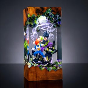 Op de afbeelding: Een rechthoekige hars- en houten bloklamp met twee anime-figuren in een gevechtshouding. E&eacute;n figuur heeft stekelig oranje haar en een blauw-wit pak, terwijl de andere donker haar en een groen-paarse outfit heeft, omringd door wervelende witte rook.