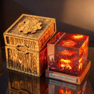May include: A wooden box with a Vault Boy emblem on the lid next to a square resin lamp featuring a glowing mushroom cloud explosion over a city, with a metal plaque at the base displaying the text "WAR NEVER CHANGES" in capital letters.
