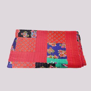 Op de afbeelding: Een gevouwen patchwork quilt met diverse kleurrijke patronen. De quilt toont rode, zwarte, blauwe en groene secties met bloemen- en geometrische ontwerpen. De quilt lijkt van katoen te zijn.