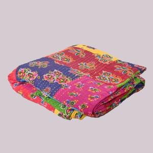 May include: Folded patchwork quilt with floral patterns in shades of red, pink, blue, and yellow. The quilt features a variety of floral designs and is bordered with green and blue accents. The quilt is folded and ready for use.