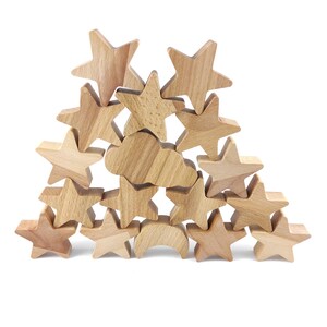 Pode incluir: Uma coleção de formas de madeira de cor clara empilhadas em forma de pirâmide. O conjunto inclui várias estrelas de cinco pontas, uma forma de nuvem e uma forma de lua crescente, todas com um acabamento liso de grão de madeira natural.