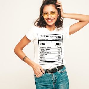 May include: White t-shirt with a black graphic of a nutrition label that reads "Birthday Girl" and lists the amount of "Fun" per serving as 1000. The label includes items like "Birthday Wishes", "Hugs & Kisses", "Happiness", "Games & Prizes", "Surprises", "Gifts", "Family", "Friends", and "Memories".