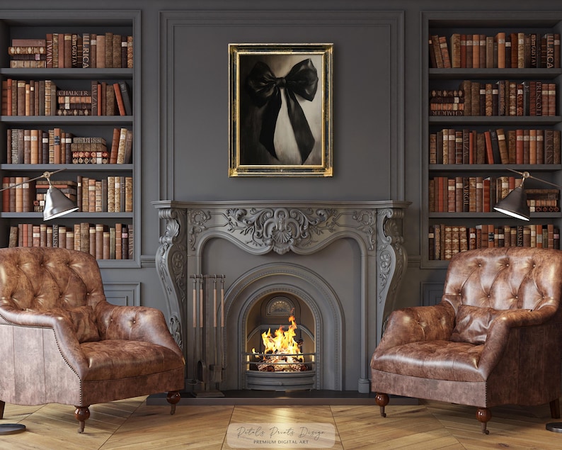 May include: A black and white bow art print in a gold frame hangs above a fireplace with a burning fire. Two brown leather armchairs flank the fireplace, and bookshelves filled with books are on either side.