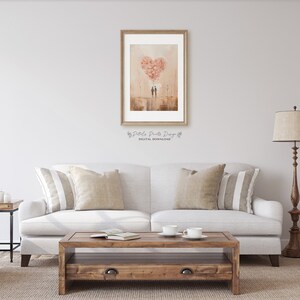 May include: A framed print of a watercolour painting depicting two figures standing beneath a large heart-shaped cloud made of pink flowers. The background is a soft, peachy colour with a hint of brown.