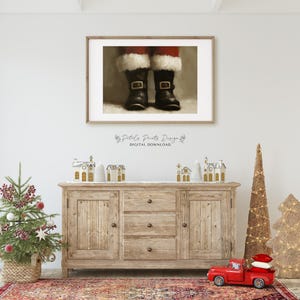 May include: A digital download of a printable art print featuring a close-up of Santa's boots. The boots are black with white fur trim and buckles. The background is a light brown color.