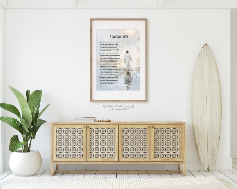 May include: A framed print with a poem titled "Footprints" about walking through life's challenges. The poem is printed on a white background with a watercolor-style image of a person walking on a beach with their footprints in the water. The image is framed in a light wood frame.