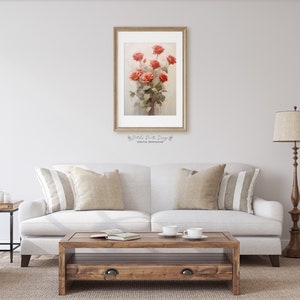 May include: A framed watercolor painting of a bouquet of red roses in a vase. The painting is hanging on a white wall above a white couch with beige pillows.