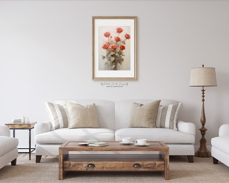 May include: A framed watercolor painting of a bouquet of red roses in a vase. The painting is hanging on a white wall above a white couch with beige pillows.