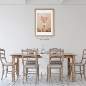 May include: A digital download of a watercolour painting depicting a couple standing under a heart-shaped balloon made of pink flowers. The painting is framed and hanging on a white wall above a wooden dining table with chairs.