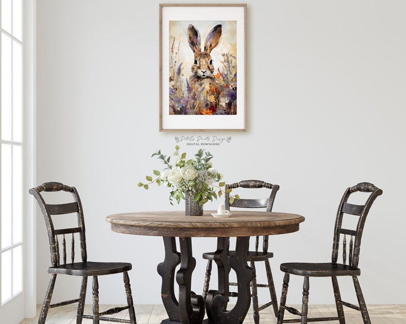 Puede incluir: Una pintura de acuarela de un conejo marr&oacute;n con orejas largas en un campo de flores silvestres p&uacute;rpuras y amarillas. La pintura est&aacute; enmarcada en un marco de madera simple y est&aacute; colgada en una pared blanca.