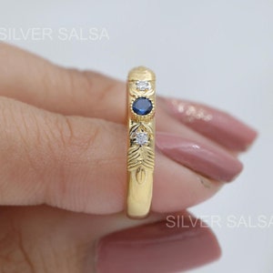 Può includere: Un anello con fascia in oro con un design di pietre preziose blu e bianche. L'anello ha un motivo floreale sulla fascia.