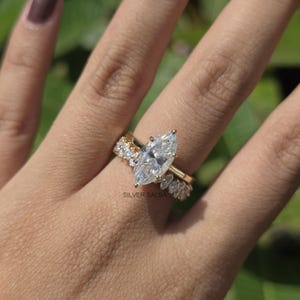 May include: A gold engagement ring with a marquise-cut diamond and a band of smaller diamonds. A matching band with small diamonds is also present. The rings are on a hand, with the brand name "SILVER SALSA" visible.
