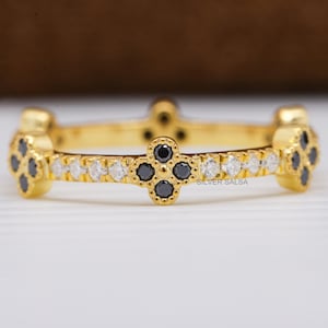 May include: A gold-toned ring with a repeating pattern of black and white gemstones. The ring features four-leaf clover-shaped designs with black stones, alternating with rows of small white stones. The words "SILVER SALSA" are visible on the ring.