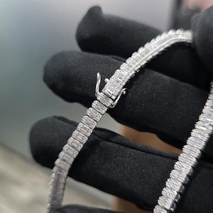 May include: A silver-colored necklace with a rectangular baguette-cut design. The necklace is being held by a gloved hand. The text "SILVER SALSA" is at the top of the image.