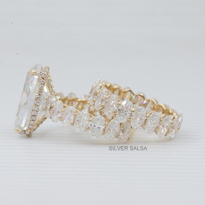 May include: A gold-toned engagement ring with a large, rectangular, clear gemstone and a halo of smaller stones. A matching band with oval-shaped stones is also present. The rings are set against a white background.