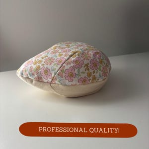 May include: A floral print newsboy cap with a light beige brim and a pink, yellow, and green floral pattern on a white background. The cap is sitting on a white surface. The text "PROFESSIONAL QUALITY!" is in a brown rectangle.