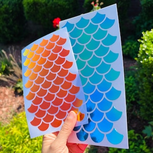 May include: Two sheets of iridescent mermaid scale stickers. One sheet is orange and the other is blue.