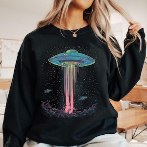May include: Black sweatshirt with a graphic of a flying saucer with a rainbow beam of light coming from it. The graphic is set against a dark blue background with stars.