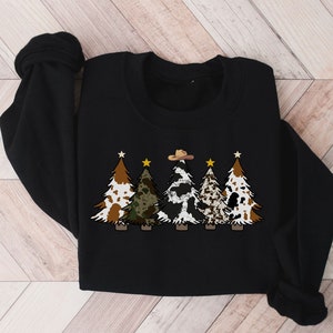 May include: Black sweatshirt featuring a design of five Christmas trees. The trees are decorated with cowhide, camouflage, and stars. The central tree is wearing a cowboy hat.