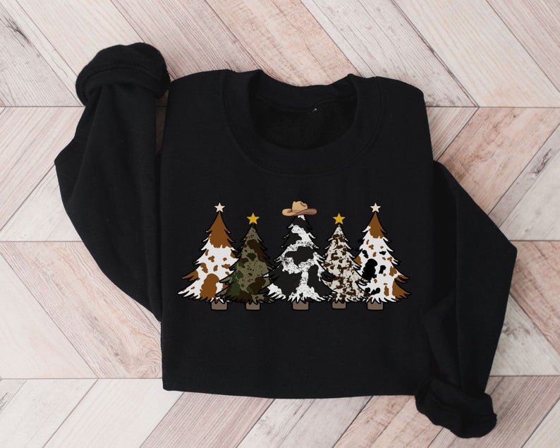 May include: Black sweatshirt featuring a design of five Christmas trees. The trees are decorated with cowhide, camouflage, and stars. The central tree is wearing a cowboy hat.