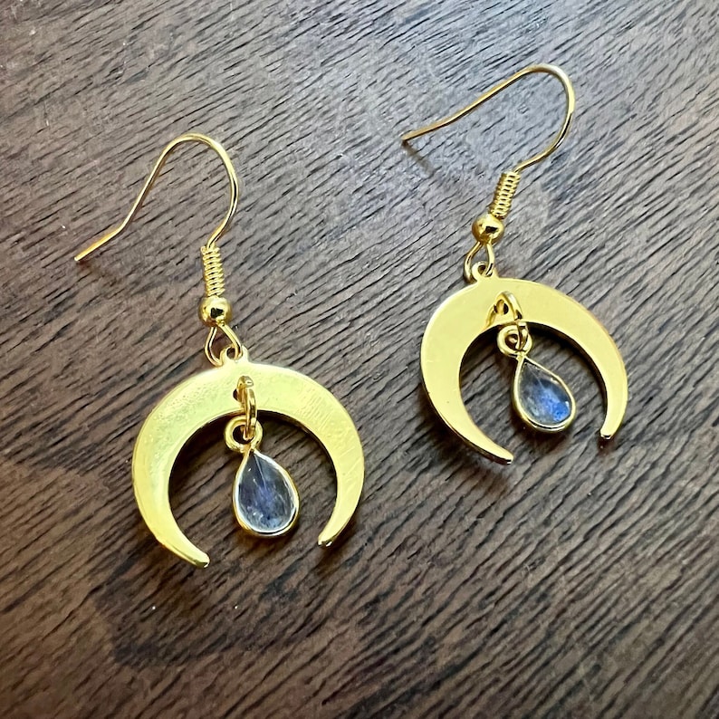 May include: A pair of gold crescent moon earrings with teardrop-shaped blue labradorite stones hanging from the bottom.
