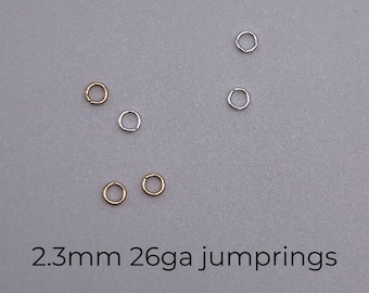 Könnte beinhalten: Nahaufnahme von sechs Sprungringen, zwei goldfarben und vier silberfarben, auf einer grauen Oberfläche. Die Sprungringe haben einen Durchmesser von 2,3 mm und eine Stärke von 26 Gauge. 2.3mm 26ga jump rings