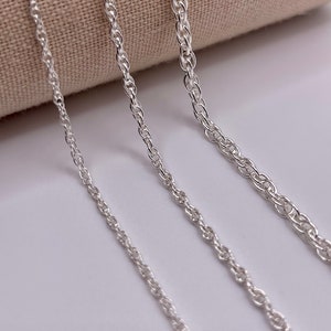May include: Three silver chains of different thicknesses, lying on a white surface. The chains are all twisted or rope style.