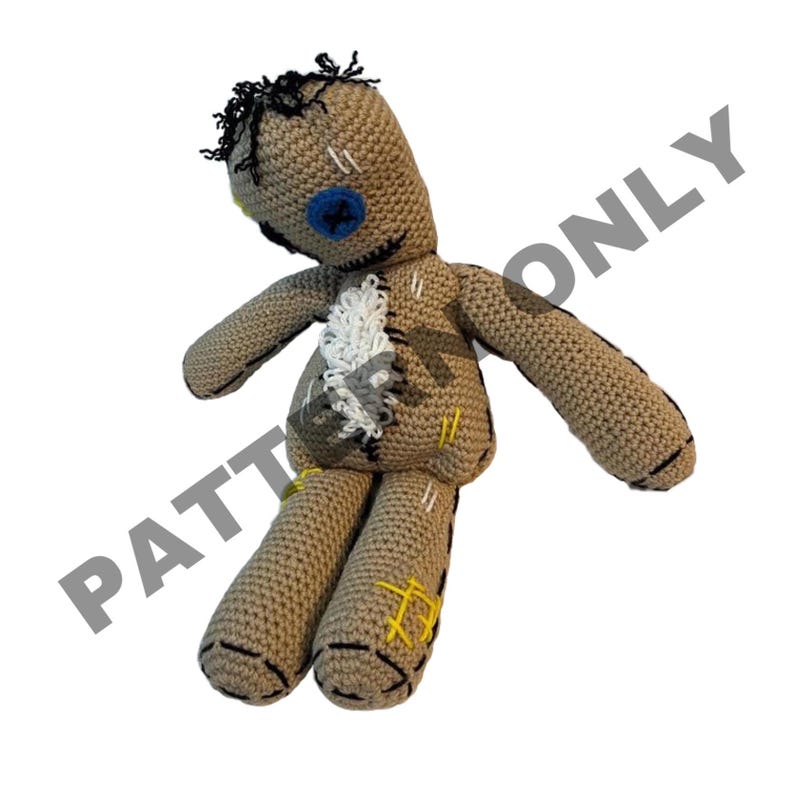 May include: A crocheted voodoo doll with a blue button eye, black hair, and brown yarn. The doll has white yarn stitches and yellow yarn accents.