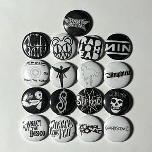 May include: A selection of sixteen black and white button badges, each displaying band logos and text. The badges feature logos for bands such as Radiohead, Nine Inch Nails, and Misfits. The badges are circular and have diverse designs.