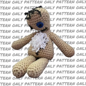 May include: A handmade crochet doll in tan yarn with black hair and stitched features. The doll has a blue eye and a white yarn accent on its chest. The arms and legs are extended, giving the doll a whimsical appearance.