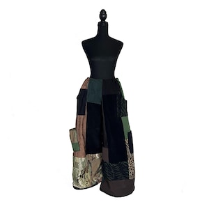 Può includere: Pantaloni patchwork in vari colori e texture, tra cui motivi neri, verdi, marroni e mimetici. I pantaloni sono esposti su un manichino nero, mostrando il design a gamba larga e le combinazioni di tessuti uniche.