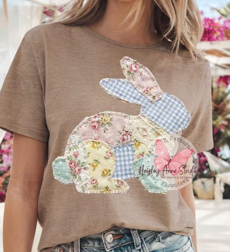 May include: A tan t-shirt featuring a patchwork bunny design. The bunny is composed of floral, gingham, and lace fabrics in pastel colors. The design includes the text "Raspberry Anne Studio" and a butterfly graphic.