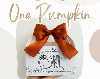 May include: A white gable box with a brown bow and the text "One Pumpkin" on the front. The box has a black and white illustration of a pumpkin with the text "Samantha is One little pumpkin" on the front.