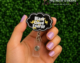 Pode incluir: Um porta-crachá em forma de nuvem preta com o texto branco Black Cloud Energy e gráficos de raios amarelos. O porta-crachá inclui uma alça de plástico transparente com um botão de pressão de metal para prender cartões de identificação.