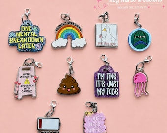 May include: A collection of ten acrylic charms with metal lobster clasps. Designs include a blue glitter sign reading ONE MENTAL BREAKDOWN LATER, a rainbow, a duck with the text GOT TOO SILLY, a green character, a pink sign reading OVER-STIMULATED APPROACH WITH CAUTION, a brown poop emoji, a purple glitter sign reading I'M FINE IT'S JUST MY FACE, a pink jellyfish, a battery icon reading I NEED A NAP, and a pink sign reading I JUST NEED COFFEE.