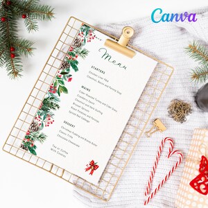 May include: A festive Christmas menu on a gold wire clipboard, adorned with a botanical border of pinecones, berries, and greenery. The menu features starters, mains, and desserts, with candy canes and a gift box nearby.